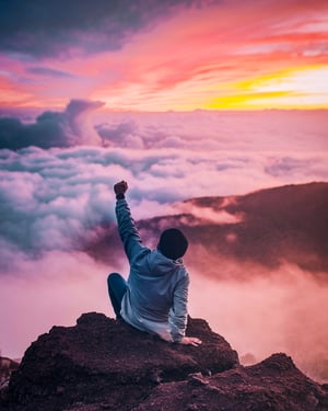 Man on mountain top, among clouds and sun with arm raised expressing victory